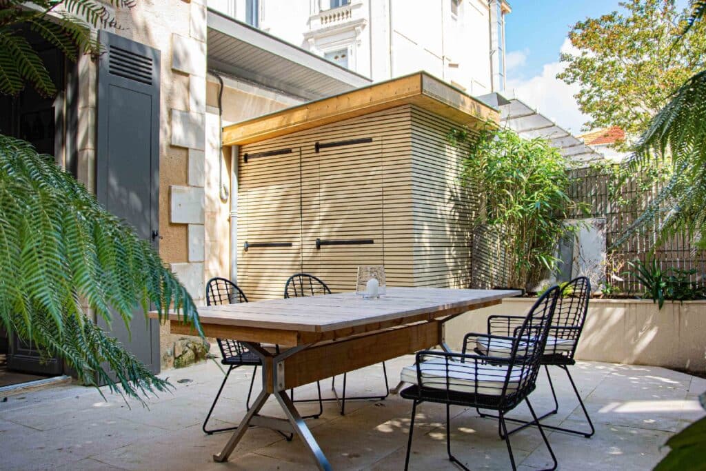 Cour intérieure végétalisée avec mobilier design et cabanon en bois, réalisée par un architecte paysagiste pour un espace extérieur moderne et apaisant.