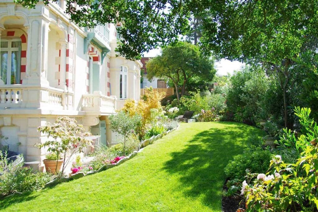 Jardin paysager d’une villa historique, alliant pelouse verdoyante, massifs fleuris et arbres majestueux pour une conception élégante et intemporelle.